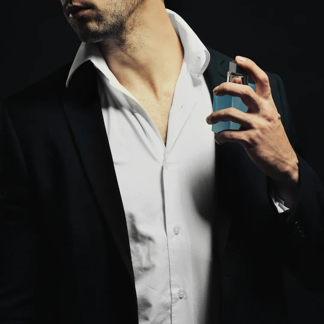 Man in a black suit and white shirt applying blue bottled perfume to his neck