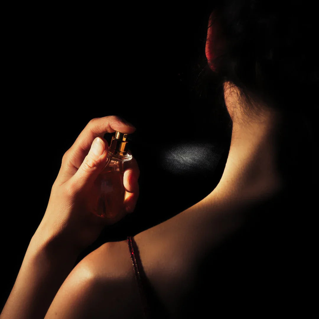 A woman applying luxury perfume to her neck in dramatic low-light lighting.